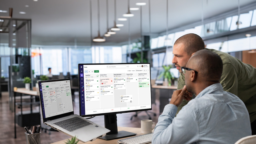 Two people at a desk looking at a pc with screen with pipedrive CRM on it